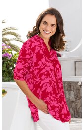 Rosa Bluse mit pinkem Blumenmuster, V-Ausschnitt, halblange Ärmel, lockere Passform, getragen von stehender Frau mit Händen in den Hosentaschen