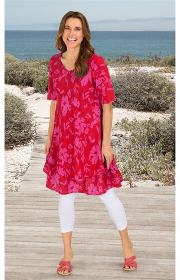 Rotes Kleid mit floralem Muster, halblange Ärmel, V-Ausschnitt, locker fallende A-Linie, getragen von stehender Frau am Strand, knielang