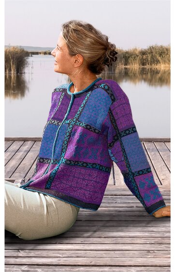 Pullover mit Kapuze in Violett und Blau, geometrisches Muster in Schwarz, langärmlig, vorne mit Kordelzug, locker geschnitten, getragen von sitzender Person seitlich gewandt auf Holzsteg am Wasser