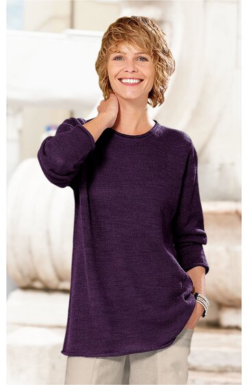 Dunkellila langärmeliges Pullover-Shirt, rundhalsausschnitt, locker geschnitten, getragen von lächelnder stehender Frau mit kurzer blonder Frisur, eine Hand im Hosenbein, helle Hose