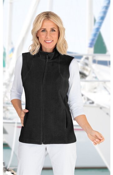Schwarze ärmellose Weste mit hohem Stehkragen, durchgehendem Reißverschluss, zwei seitlichen Taschen, getragen von lächelnder stehender Frau in weißem Dreiviertelarmshirt vor maritimem Hintergrund