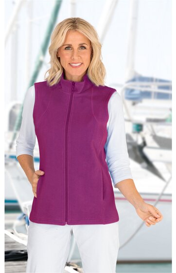 Damenweste in beerenrot, ohne Muster, Stehkragen, durchgehender Reißverschluss, zwei seitliche Eingrifftaschen, ärmellos, gerade geschnitten, getragen von stehender Frau mit weißem Langarmshirt und weißer Hose