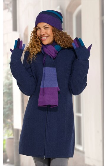 Dunkelblauer langer Wintermantel mit Reißverschluss, getragen von stehender Frau, kombiniert mit lila-blau gestreiftem Schal, lila-blau gestreifter Mütze, lila Handschuhen, schmal geschnitten