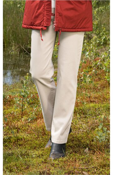 Beige lange Hose ohne Muster, gerade geschnitten, getragen von Person im Stehen, kombiniert mit schwarzen Schuhen und rotem Mantel