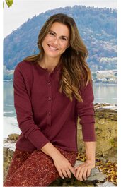 Bordeauxroter Pullover mit Knopfleiste, rundem Kragen, lange Ärmel, getragen von sitzender Frau mit langen braunen Haaren vor Berg- und Seelandschaft