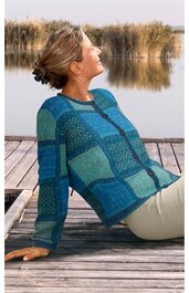 Frau sitzt entspannt auf einem Steg am Wasser, trägt einen blauen Pullover