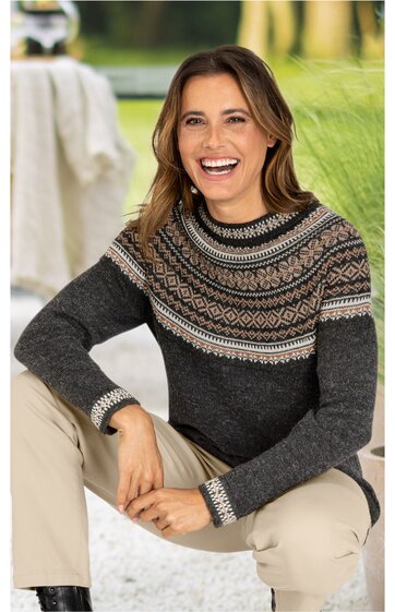 Damenpullover dunkelgrau mit mehrfarbigem Norwegermuster in Beige und Braun, Rundhalsausschnitt, lange Ärmel, getragen von sitzender Frau mit hellen Hosen
