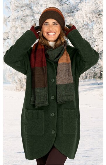 Dunkelgrüner Mantel mit großen Taschen, Knopfleiste, knielang, getragen von stehender lächelnder Frau mit brauner Mütze, dunkelrotem Schal mit orange und grauen Querstreifen, braune Handschuhe, Winterlandschaft im Hintergrund