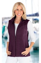 Dunkelviolette Damenweste ohne Ärmel, durchgehender Reißverschluss, Stehkragen, schmale Passform, getragen von lächelnder stehender Frau mit weißen, langärmligen Shirt und heller Hose