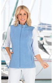 Hellblaue ärmellose Weste mit Stehkragen, durchgehendem Reißverschluss, zwei seitlichen Eingrifftaschen, getragen von stehender Frau mit weißem Dreiviertelarmshirt und weißer Hose vor Hafenhintergrund