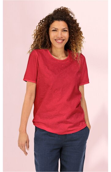 Rotes T-Shirt ohne Muster, rundhalsausschnitt, kurze Ärmel, gerade geschnitten, getragen von stehender Frau mit lockigem Haar, Hände locker an den Seiten, kombiniert mit dunkelblauen Hosen