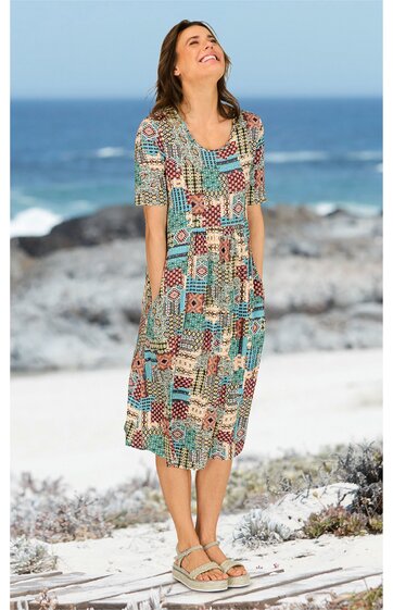 Midikleid in Türkis mit abstraktem Patchworkmuster in Rot, Beige und Braun, rundhals, halblange Ärmel, taillierter Schnitt, getragen von stehender Frau am Strand, fließender Stoff