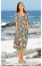 Midikleid in Türkis mit abstraktem Patchworkmuster in Rot, Beige und Braun, rundhals, halblange Ärmel, taillierter Schnitt, getragen von stehender Frau am Strand, fließender Stoff