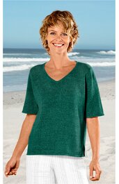 Damenpullover in dunklem Tannengrün, unifarben, V-Ausschnitt, kurze Ärmel, gerade geschnittener Saum mit kleinen seitlichen Schlitzen, getragen von lächelnder, stehender Frau am Strand