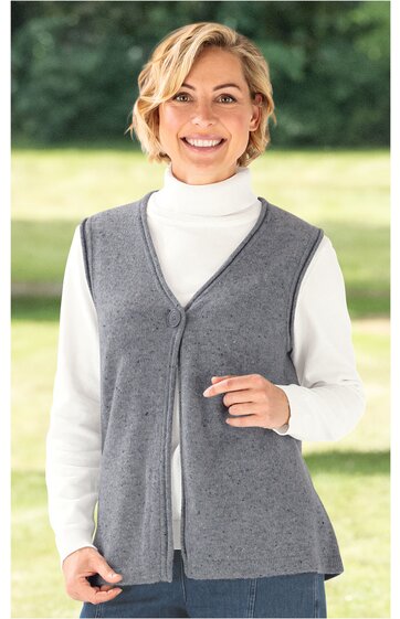 Graue ärmellose Strickweste mit V-Ausschnitt und durchgehendem Reißverschluss vorne, getragen von lächelnder Frau im Stehen, darunter weißer Rollkragenpullover, gerade geschnitten