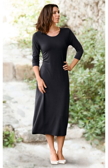 Schwarzes, knöchellanges Kleid mit 3/4-Ärmeln, rundem Ausschnitt, schmaler Passform, getragen von einer stehenden Frau mit linker Hand in der Hüfte und rechter Hand am Rock, schlichte, gerade Form