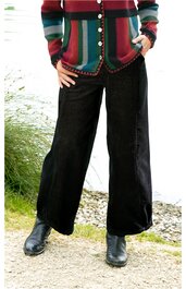 Schwarze, weite Hose mit geradem Bein, hohe Taille, getragen von stehender Person mit Händen in den Taschen, kombiniert mit langärmligem, gestreiftem Cardigan in Grün-, Rot- und Beigetönen, schwarze Lederstiefel