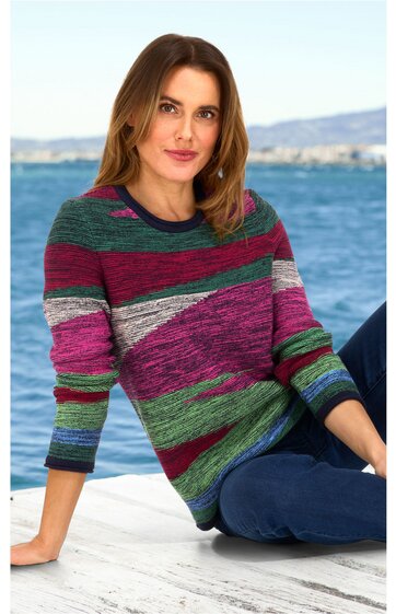 Pullover mit Rundhalsausschnitt, mehrfarbig gestreift in Tönen von Grün, Bordeaux, Pink, Grau und Blau, lange Ärmel, getragen von sitzender Frau mit lockeren blonden Haaren, kombiniert mit blauer Hose