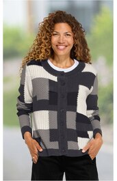 Strickjacke in Schwarz, Weiß und Grautönen mit großem geometrischem Karomuster, Rundhalsausschnitt, Knopfleiste, lange Ärmel, gerade geschnitten, getragen von lächelnder Frau in stehender Pose, Hände in den Taschen