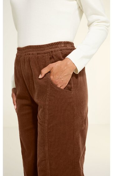 Braune Hose mit elastischem Bund, seitlichen Taschen, gerade geschnitten, getragen von stehender Person mit weißem langärmligem Oberteil