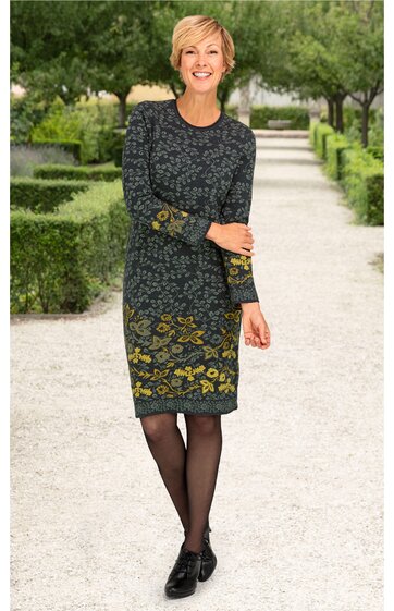 Dunkelgrünes Kleid mit gelbem Blumenmuster, langärmlig, rundhalsausschnitt, knieumspielend, gerade geschnitten, getragen von stehender Frau, schwarze Schuhe, schwarze Strumpfhose