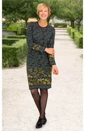 Dunkelgrünes Kleid mit gelbem Blumenmuster, langärmlig, rundhalsausschnitt, knieumspielend, gerade geschnitten, getragen von stehender Frau, schwarze Schuhe, schwarze Strumpfhose