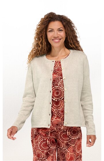 Beige langärmelige Strickjacke, rundhals, durchgehende Knopfleiste, getragen von lächelnder stehender Frau mit offenen Haaren, darunter rot gemustertes Kleid mit Kreis- und Punktmustern
