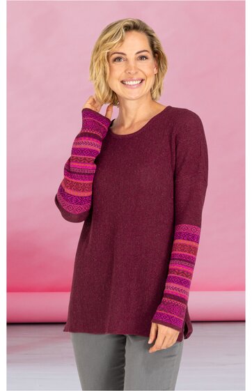 Lang geschnittenes Pulloverkleid in dunklem Weinrot, Ärmel mit breiten, horizontalen Streifen in Pink und Lila, Rundhalsausschnitt, getragen von lächelnder stehender Frau mit kurzen blonden Haaren
