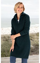 Dunkelgrüner Strickpullover-Kleid, langer Schnitt, Stehkragen mit Reißverschluss, geripptes Muster an Ärmeln und Kragen, lange Ärmel, getragen von lächelnder stehender Frau vor Strandkulisse