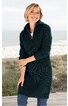 Dunkelgrüner Strickpullover-Kleid, langer Schnitt, Stehkragen mit Reißverschluss, geripptes Muster an Ärmeln und Kragen, lange Ärmel, getragen von lächelnder stehender Frau vor Strandkulisse