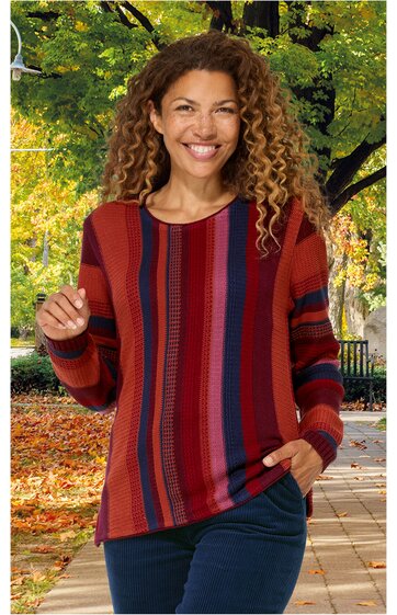 Pullover in Rostrot mit verschiedenen breiten senkrechten Streifen in Dunkelrot, Blau und Schwarz, Rundhalsausschnitt, lange Ärmel, getragen von lächelnder Frau mit lockigen Haaren, stehende Pose, locker geschnitten