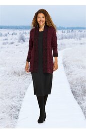 Langärmeliger bordeauxroter Cardigan mit offenem Schnitt, getragen von Frau mit lockigen Haaren, kombiniert mit schwarzem knielangem Kleid, schwarzer Strumpfhose und schwarzen Schuhen, stehende Pose auf weißem Weg vor schneebedeckter Landschaft