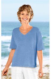 Hellblaues Kurzarmshirt mit V-Ausschnitt, gerade geschnitten, seitliche Schlitze am Saum, getragen von lächelnder Frau stehend vor Meereskulisse