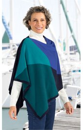 Poncho in Blau- und Grüntönen mit geometrischem Muster, lockere Form ohne Kragen, offen geschnitten, getragen von stehendem Menschen mit weißen Rollkragenpullover und blauen Jeans