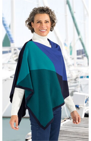 Poncho in Blau- und Grüntönen mit geometrischem Muster, lockere Form ohne Kragen, offen geschnitten, getragen von stehendem Menschen mit weißen Rollkragenpullover und blauen Jeans