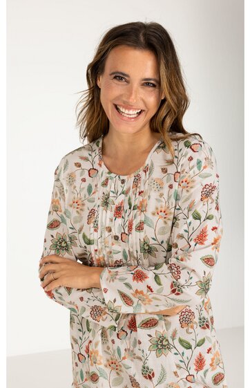 Weißes, langärmeliges Kleid mit buntem Blumenmuster, Rundhalsausschnitt, Knopfleiste vorne, leichte Falten an der Brust, lange Ärmel mit Manschetten, getragen von lächelnder stehender Frau mit verschränkten Armen