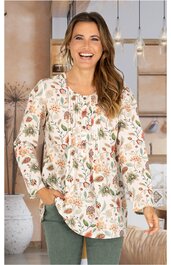 Locker geschnittene, cremeweiße Bluse mit buntem Blumenmuster, langer Ärmel, Rundhalsausschnitt mit kleiner Knopfleiste vorne, getragen von lächelnder, stehender Frau mit offener Haltung