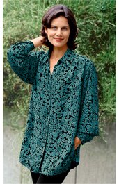 Locker geschnittene Tunika in dunklem Petrol mit schwarzem floralen Muster, V-Ausschnitt, lange weite Ärmel, durchgehende Knopfleiste, getragen von stehender Frau mit handnah an den Kopf gelegt