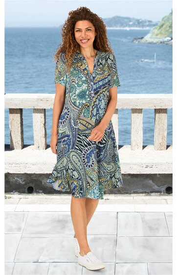 Knielanges Kleid mit Paisley-Muster in Blau- und Grüntönen, Kragen, kurzer Knopfleiste, tailliert, kurze Ärmel, getragen von stehender Frau vor Meereshintergrund