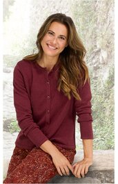 Bordeauxroter Damenstrickcardigan, langärmlig, rundhalsausschnitt, durchgeknöpft, feine Strickstruktur, getragen von sitzender Frau mit braunen, gemusterten Hosen, entspannte Pose