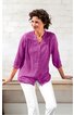 Langärmlige Bluse in violett mit Spitzenbesatz am Oberteil, durchgehender Knopfleiste, Stehkragen, locker sitzend, getragen von sitzender Frau mit weißen Hosen