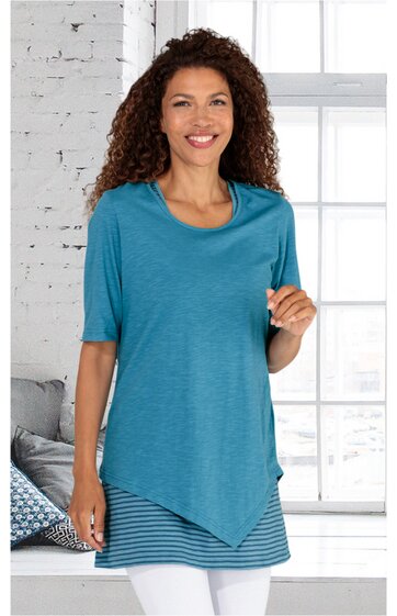 Türkisblaues Longshirt mit halbtransparentem, gestreiftem Unterteil in Dunkelblau, U-Ausschnitt, kurze Ärmel, asymmetrischer Saum, getragen von stehender Frau mit lockigen Haaren