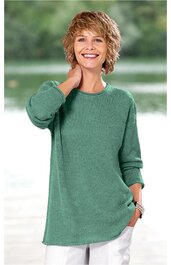 Lockeres, langärmliges T-Shirt in grün, rundhalsausschnitt, asymmetrischer Saum, getragen von stehender Frau mit Hand am Hals, Halskette und Armband sichtbar