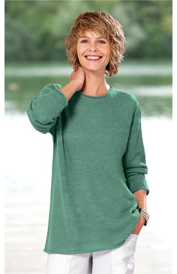 Lockeres, langärmliges T-Shirt in grün, rundhalsausschnitt, asymmetrischer Saum, getragen von stehender Frau mit Hand am Hals, Halskette und Armband sichtbar