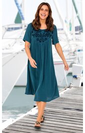 Dunkelpetrolfarbenes Midikleid mit schwarzen Blumenstickereien auf der Brust, rundem Ausschnitt, kurzen Ärmeln, lockerer Schnitt, getragen von lächelnder stehender Frau, flache Sandalen