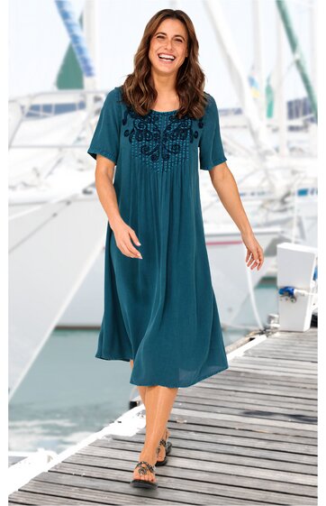 Dunkelpetrolfarbenes Midikleid mit schwarzen Blumenstickereien auf der Brust, rundem Ausschnitt, kurzen Ärmeln, lockerer Schnitt, getragen von lächelnder stehender Frau, flache Sandalen