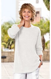 Helles, einfarbiges Longsleeve, hellelfenbein, rundhalsausschnitt, lange Ärmel, gerade geschnitten, getragen von lächelnder stehender Frau mit kurz gelocktem blondem Haar, rechte Hand im Haar, linke Hand in Hosentasche