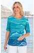 Damen-Shirt türkis mit weißen, wellenförmigen Linien, halblange Ärmel, Rundhalsausschnitt, gerade geschnitten, getragen von stehender Frau vor Wasser und Felskulisse