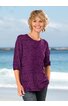Lila Pullover mit breitem Rundhalsausschnitt, 3/4-Ärmeln, horizontale Streifenstruktur, lockere Passform, getragen von lächelnder stehender Frau, gerader Saum, Taschen an der Seite
