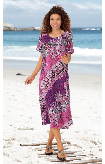 Knielanges Kleid mit halblangen Ärmeln, lila Grundfarbe, pinkes und weißes Paisley-Muster, Rundhalsausschnitt, gerade Form, getragen von lächelnder stehender Frau am Strand